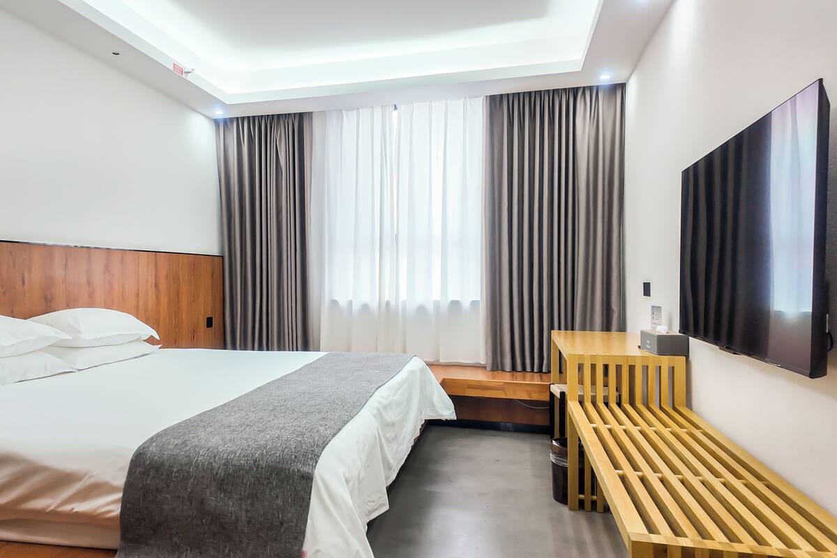 A hotel room with a bed, a desk, a chair, a TV, and a window with curtains.
