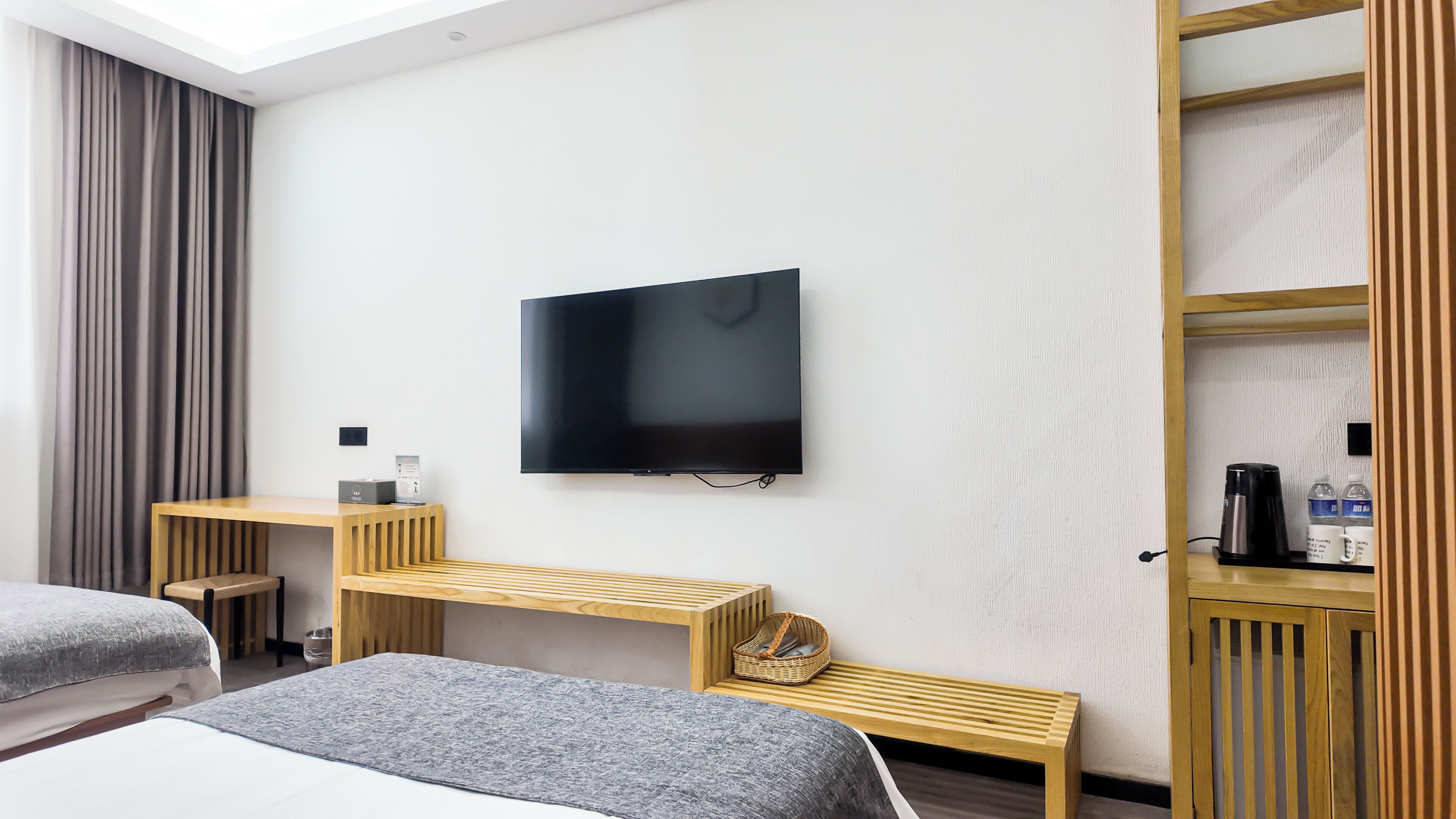 Habitació d'hotel amb un llit, televisió penjada a la paret, escriptori de fusta, una panxa i una estant amb productes d'higiene.
