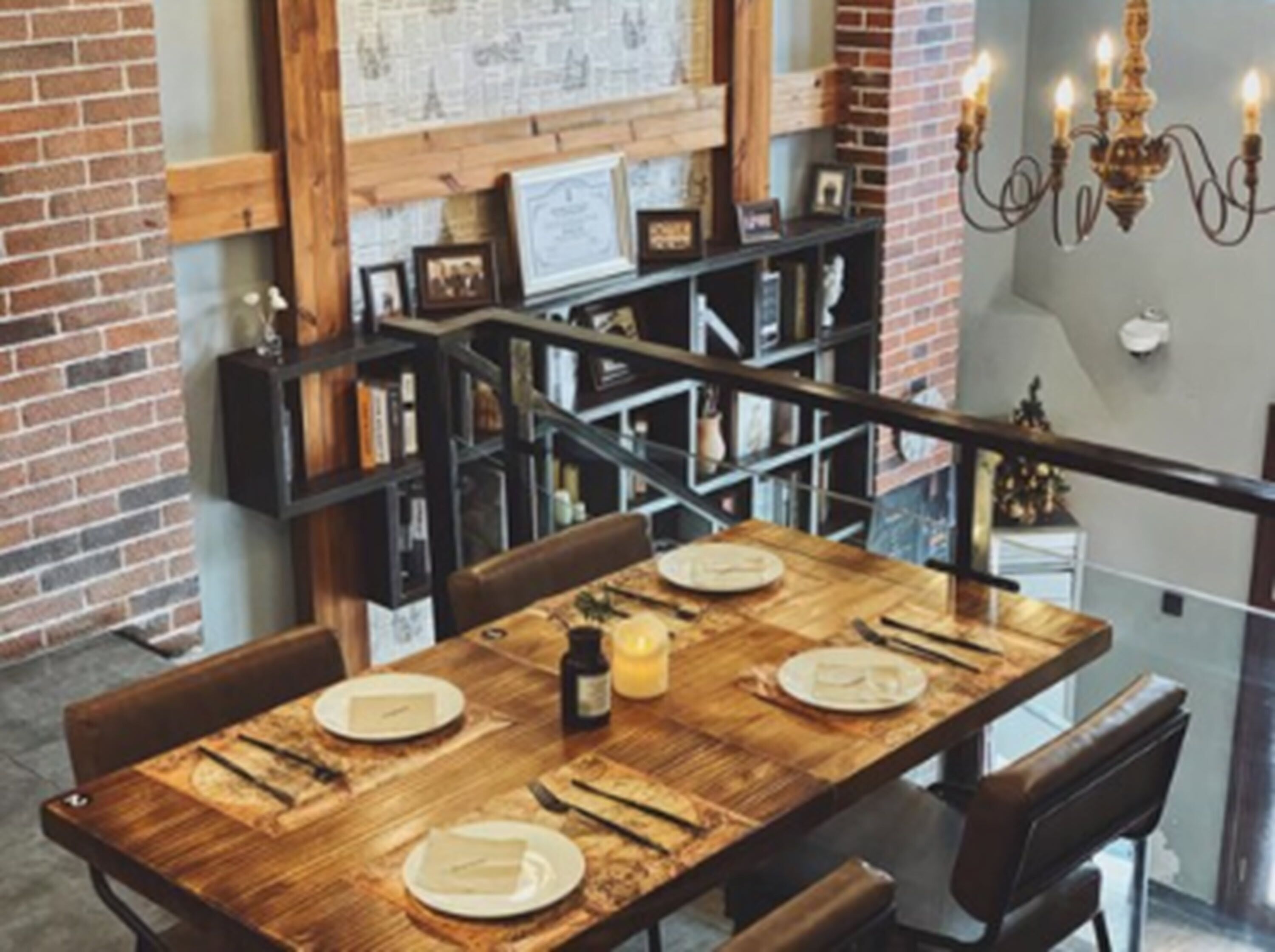 A dining area with a wooden table set for four, a brick wall, and a staircase with a railing.