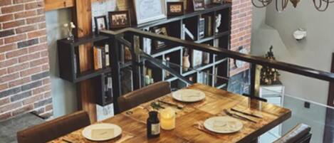 A dining area with a wooden table set for four, a brick wall, and a staircase with a railing.
