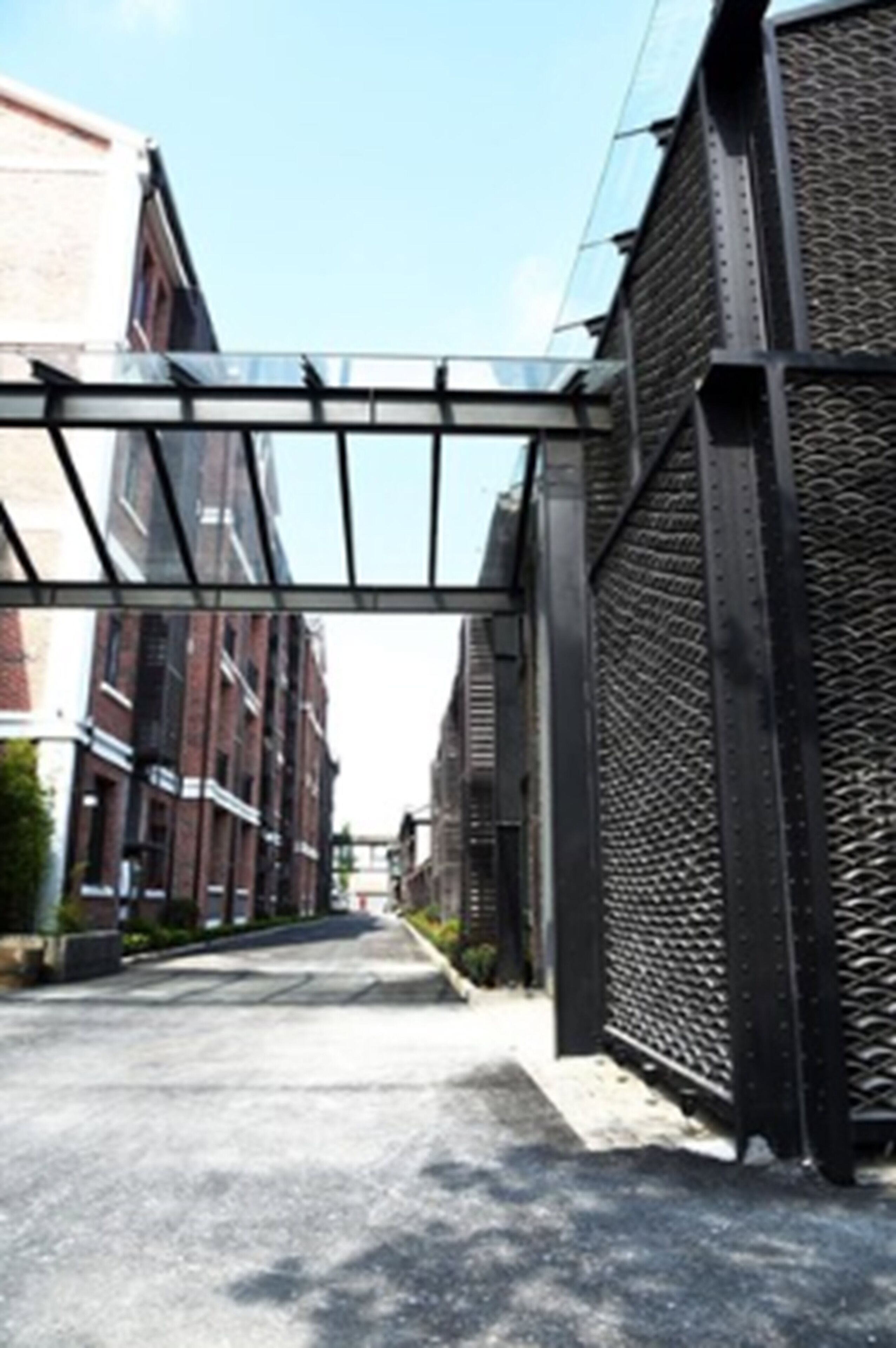 A modern urban street with a metal bridge structure, brick buildings, and a clear sky.