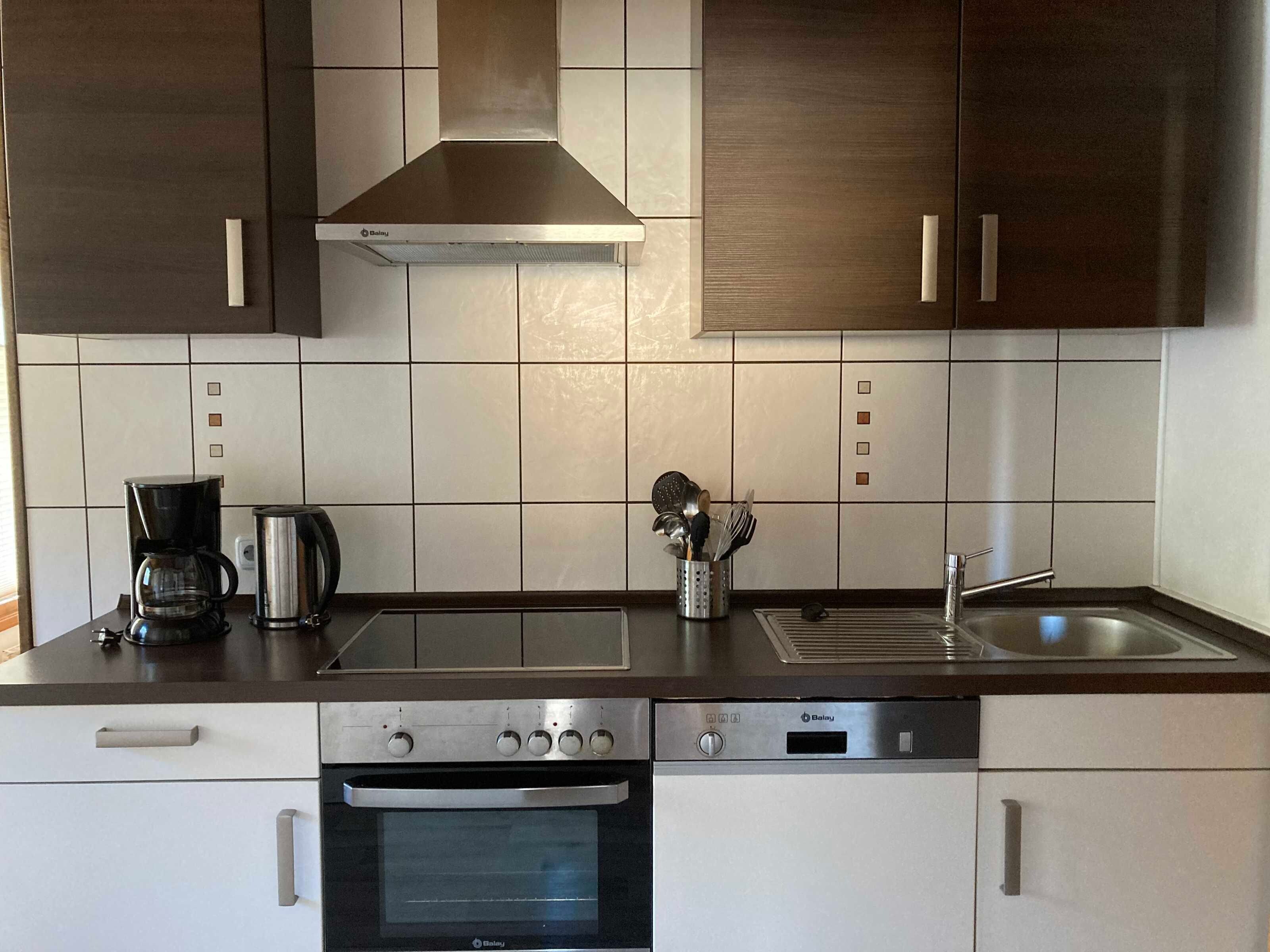 A modern kitchen with a stove, oven, coffee maker, and a range hood.