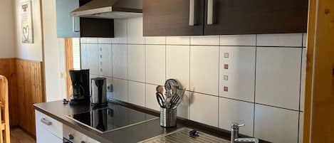 Una cocina moderna con horno empotrado, cafetera, pileta y un organizador de utensilios.