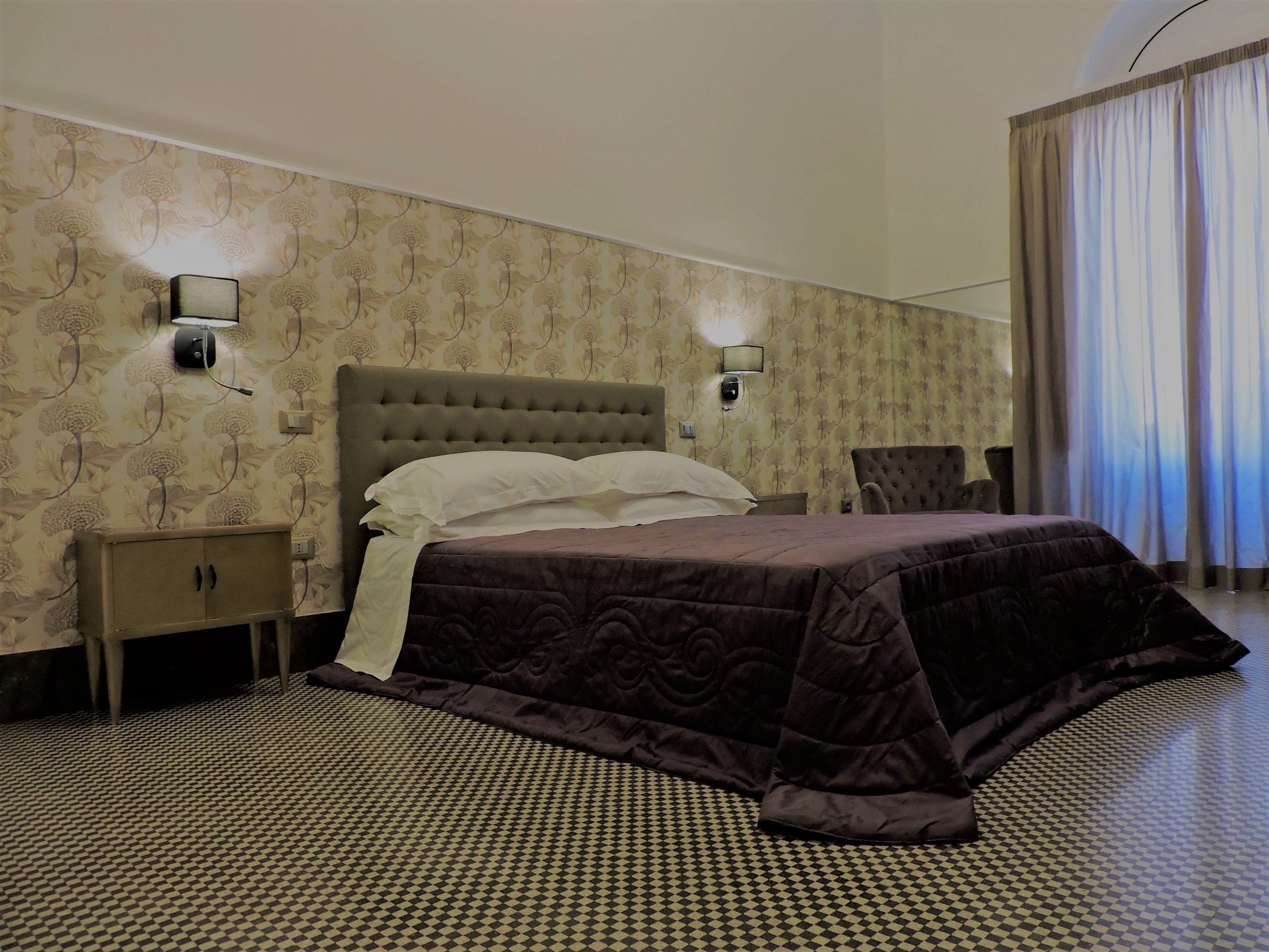 Ein Hotelzimmer mit einem großen Bett, zwei Nachttischen, einem Sessel und einer Wand mit Muster.