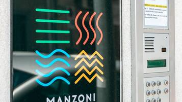 Entrada de l'hotel aparthotel Manzoni Elements, amb un teclat numèric i una porta de vidre que mostra el logotip.