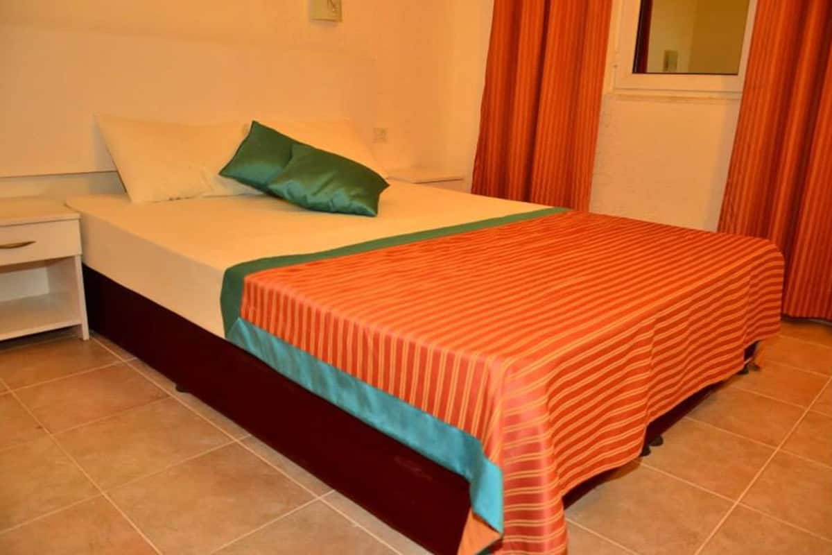 A single bed with a striped bedspread, a green pillow, and a nightstand with a drawer.