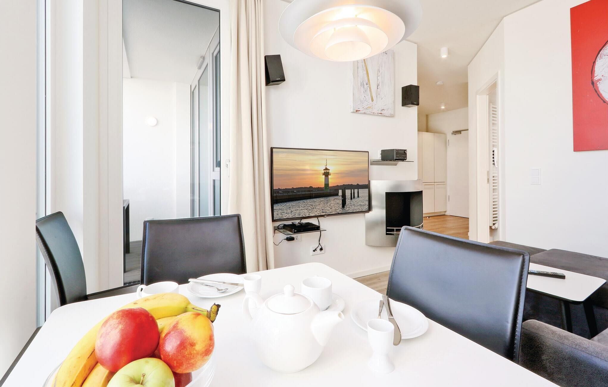 Een eethoek met een tafel gedekt voor twee personen, inclusief een fruitschaal, een witte theepot, kopjes en een bord.