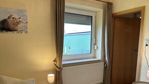 Ein Schlafzimmer mit Fenster, Nachttisch mit Lampe, Holztür und Heizkörper.