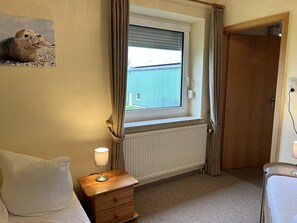 Ein Schlafzimmer mit Fenster, Nachttisch mit Lampe, Holztür und Heizkörper.
