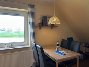 Ein Essbereich mit Tisch, Stühlen, einer Hängelampe, einem Fenster mit Blick auf Grünflächen und einer Heizung.