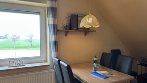 Ein Essbereich mit Tisch, Stühlen, einer Hängelampe, einem Fenster mit Blick auf Grünflächen und einer Heizung.