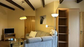 Ein Wohnzimmer mit einer Couch, einem Glastisch, einem Fernseher, einer Holztür und einer Lampe.