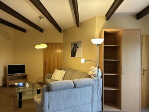 Ein Wohnzimmer mit einer Couch, einem Glastisch, einem Fernseher, einer Holztür und einer Lampe.