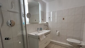 Ein modernes Badezimmer mit Duschkabine aus Glas, einem weißen Waschbecken mit Handtuch und einer Toilette.