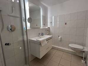 Um banheiro moderno com box de vidro, pia branca com toalha e vaso sanitário.