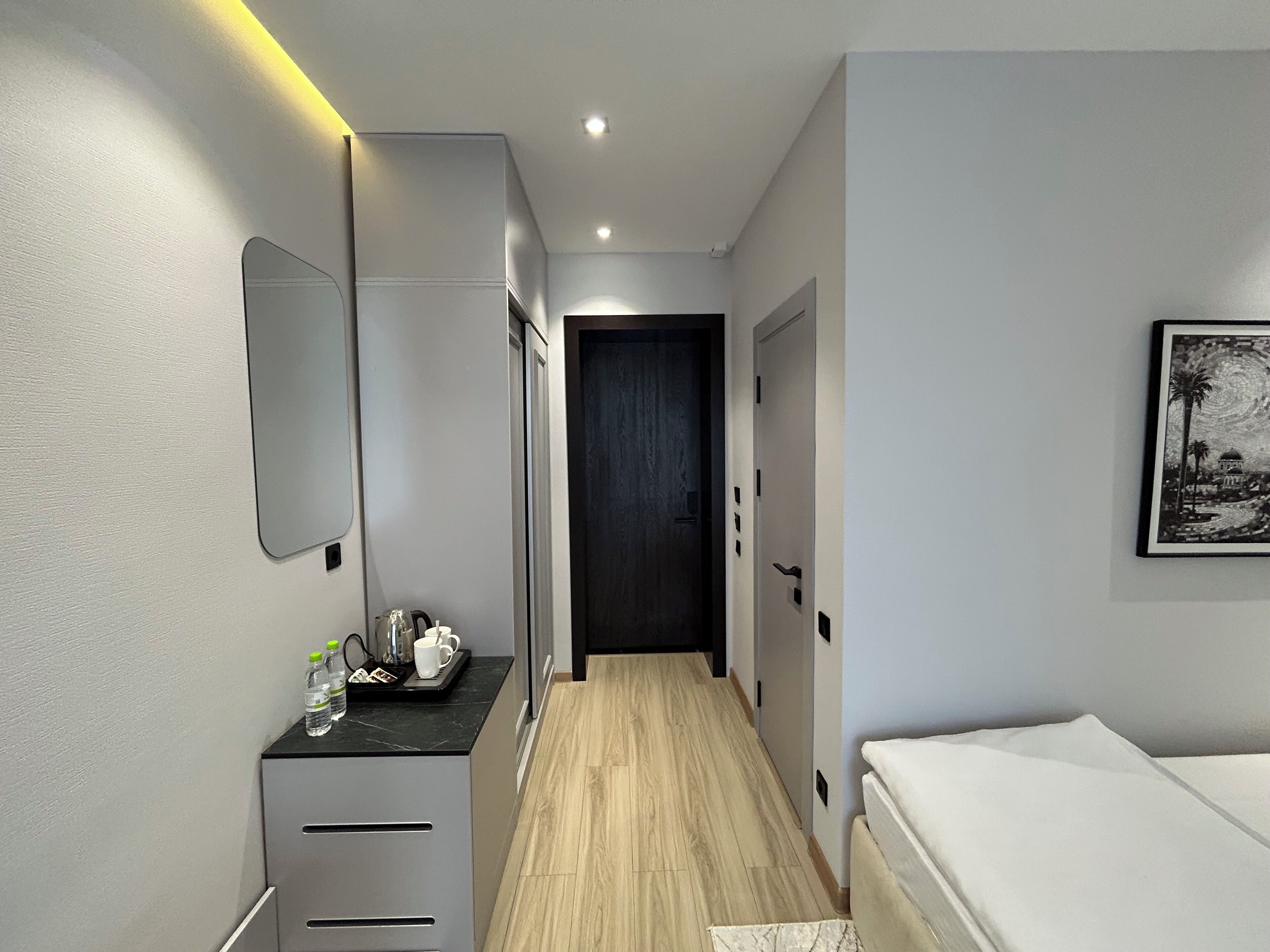 A modern hotel room with a bed, a desk with a mirror, and a framed picture on the wall.