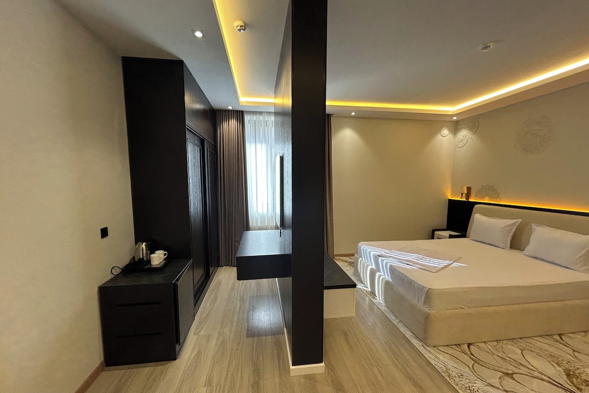 Una habitación de hotel moderna con una cama grande, una mesita de noche, un espejo y un armario.