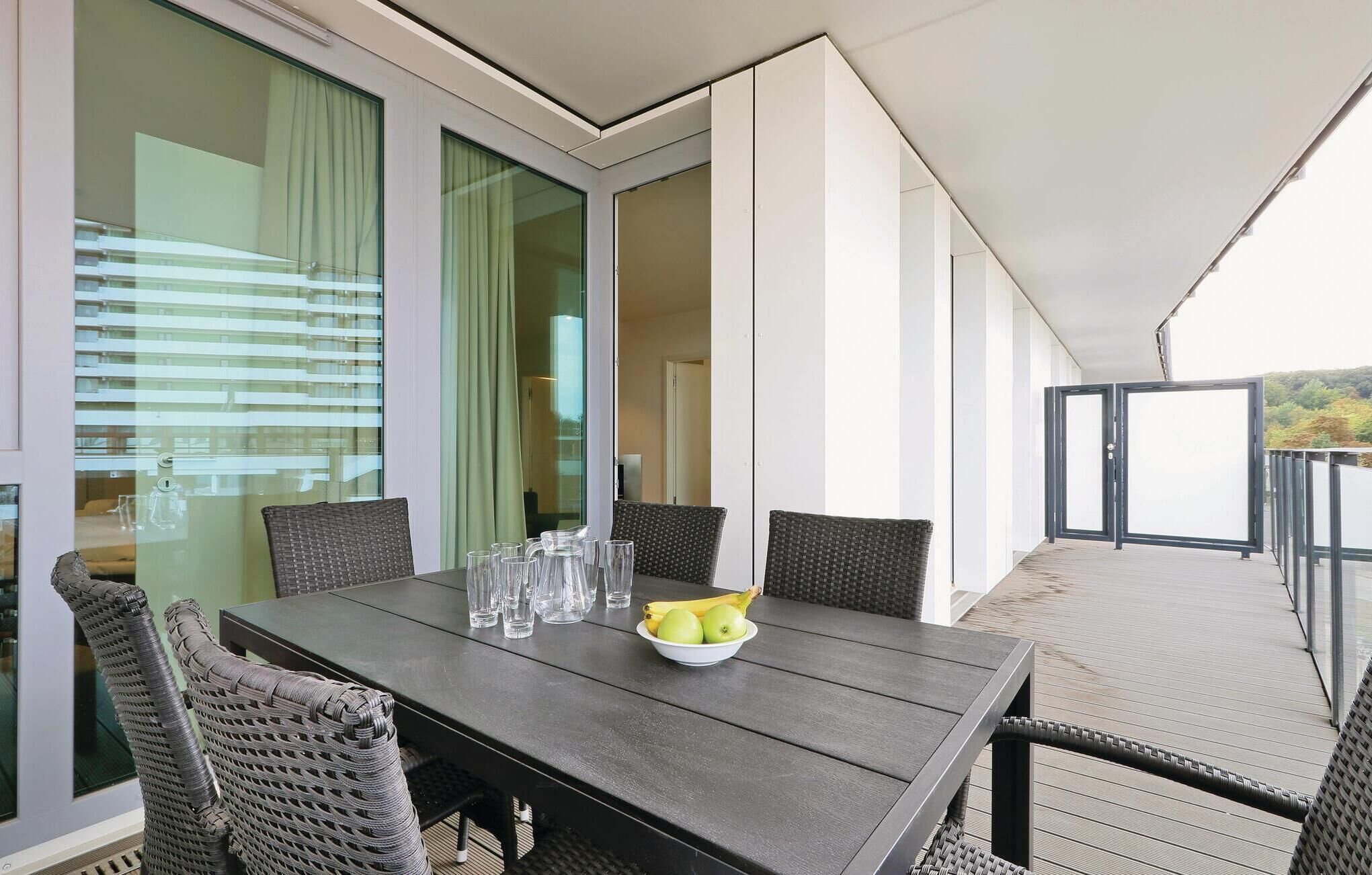 Un espacio al aire libre moderno con zona de comedor, una mesa y sillas, un cuenco con fruta y vasos transparentes.