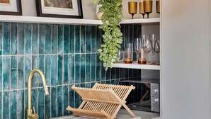 A kitchen with a white sink, a gold faucet, teal backsplash tiles, framed pictures on the wall, a hanging plant, and a microwave on the counter. - 66 Keerom 521 (Cape Town)