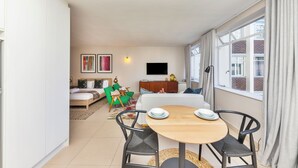 A modern living room with a dining area, a sofa set, a flat-screen TV mounted on the wall, and a large window with curtains. - 66 Keerom 521 (Cape Town)
