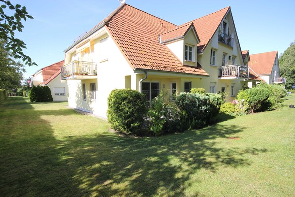 Uma casa de dois andares com telhado de telhas vermelhas, uma varanda no segundo andar e um gramado bem cuidado.