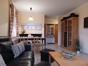 A living room with a sofa, a dining table with chairs, a wooden cabinet, and a hanging light fixture.