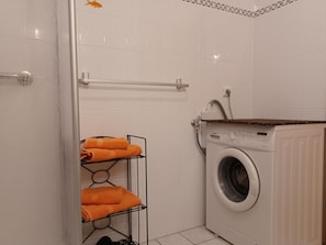 Et lille, rent vaskerum med vaskemaskine, et metalstativ med håndklæder og en hvid flisevæg.
