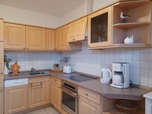 Une cuisine avec des meubles de rangement en bois, un lave-vaisselle, un four, une machine à café et une étagère ornée d’une statuette d’oiseau.