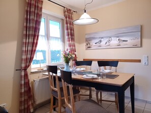 A dining area with a table set for two, a vase of flowers, and a painting of birds on the wall.