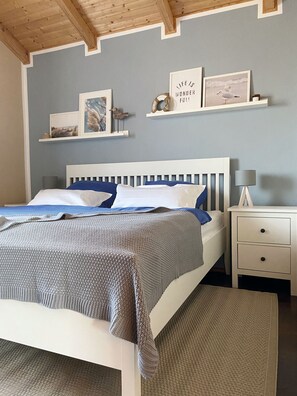 Quarto com cama, mesas de cabeceira e prateleiras fixadas na parede com objetos decorativos.