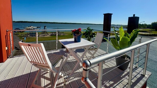 Un balcone con tavolo e sedie, con vista su un corso d'acqua con barche e un molo.
