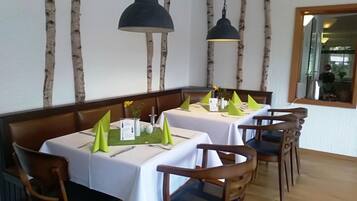 Interior de un restaurante con paredes con motivos de abedul, sillas y mesas de madera, y servilletas y menús verdes.
