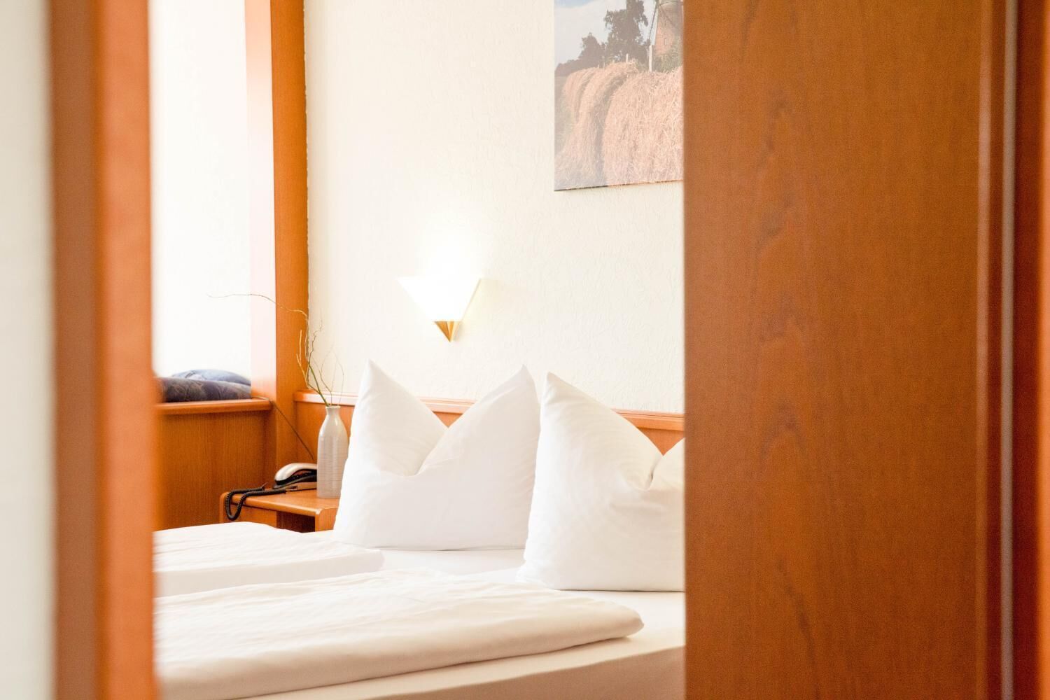 Una habitación de hotel con una cama bien hecha, una lámpara de noche y un cuadro en la pared.