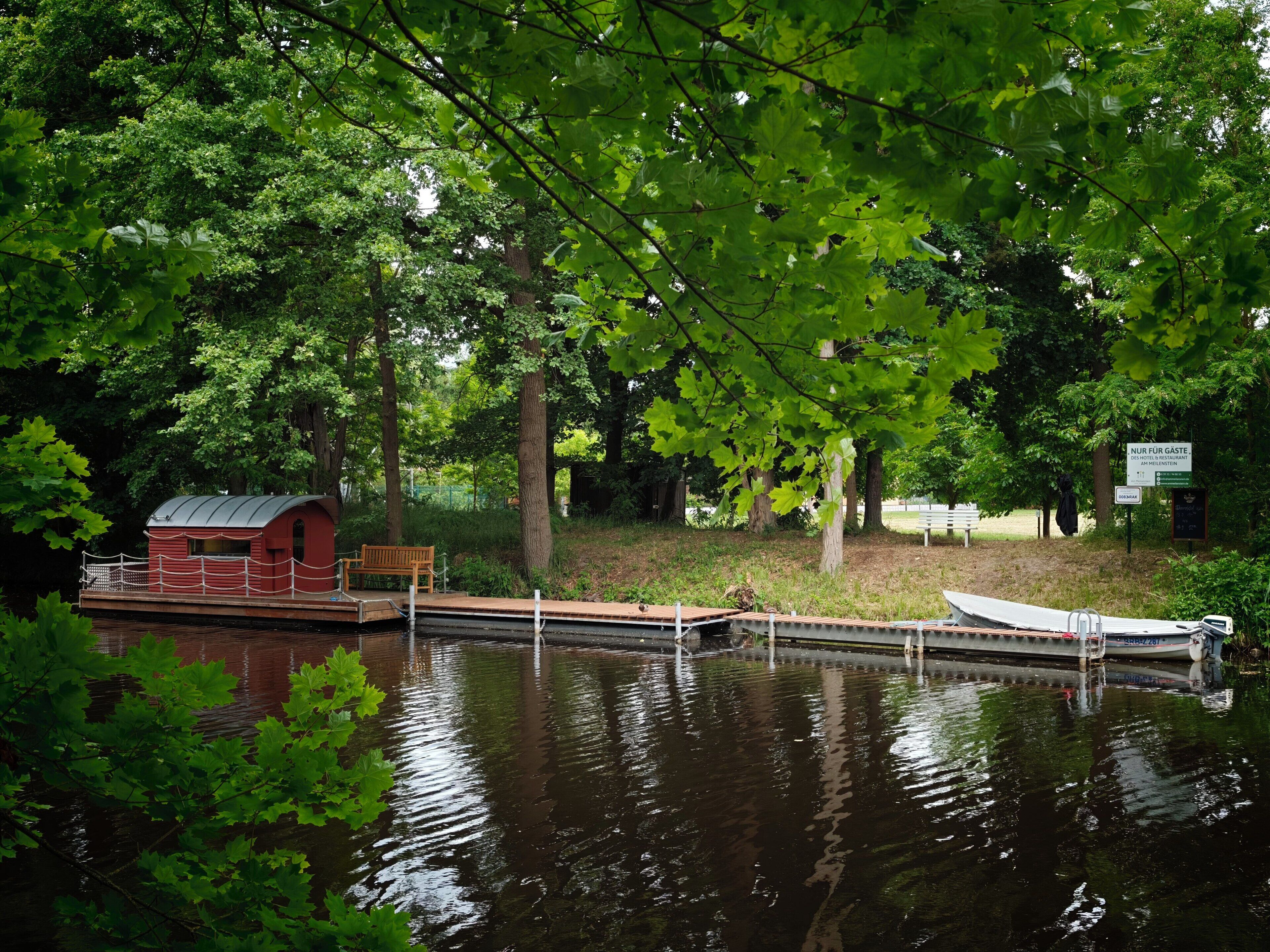 A riverside cabin with a dock, surrounded by trees and greenery.