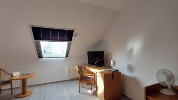 A small, well-lit room with a desk, chair, television, and a mirror.
