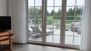 A room with a large sliding glass door leading to an outdoor deck with lounge chairs and a barbecue grill. - Craft Berry GmbH Hotel and Restaurant at the Milestone (Jerichow)