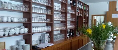 Una cocina bien organizada con estantes llenos de cristalería y botellas, una encimera de madera con un florero y un lavamanos.