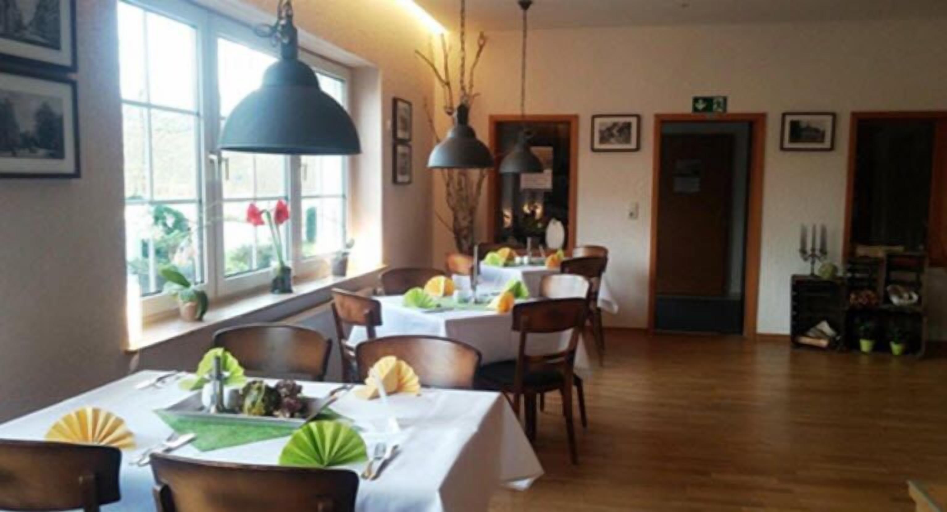 A dining area with tables set for meals, wooden flooring, and pendant lighting.