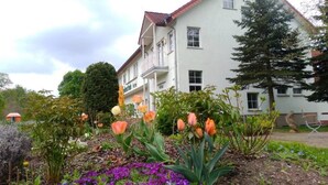 A two-story building with a balcony, surrounded by a garden with various plants and flowers. - Craft Berry GmbH Hotel and Restaurant at the Milestone (Jerichow)