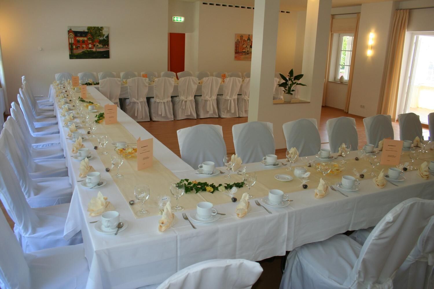 Una larga mesa de banquete dispuesta para un evento formal, con manteles blancos, sillas a juego y un montaje de platos ordenado.