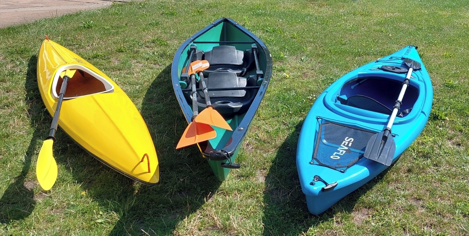 Three kayaks on grass.