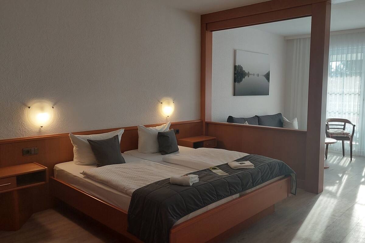 A hotel room with a large bed, bedside tables, a mirror, and a view of a balcony.