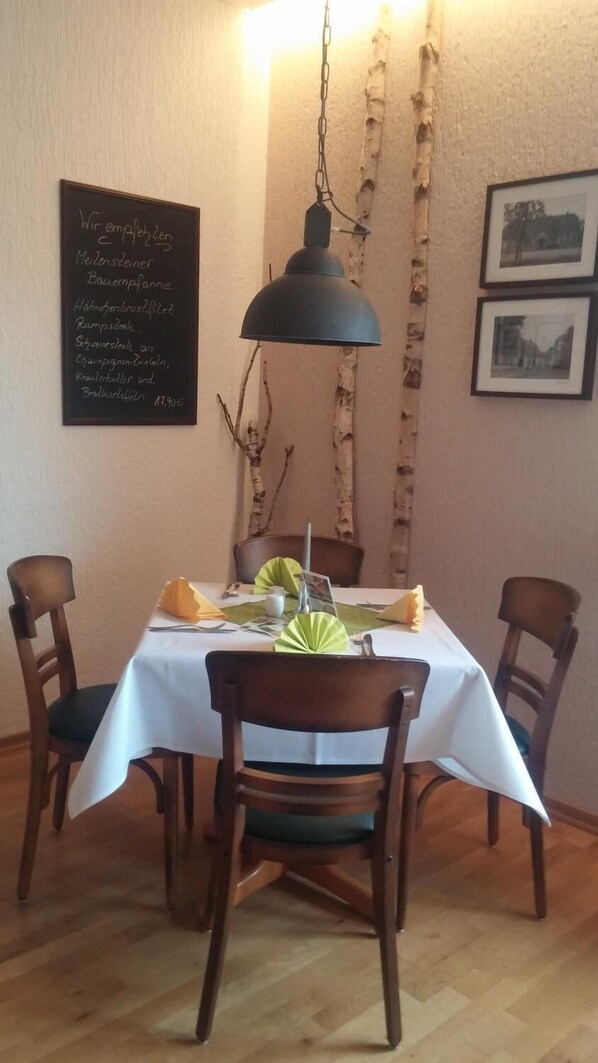Un comedor con una mesa preparada para cuatro personas, una lámpara colgante, ramas de abedul y cuadros en la pared.