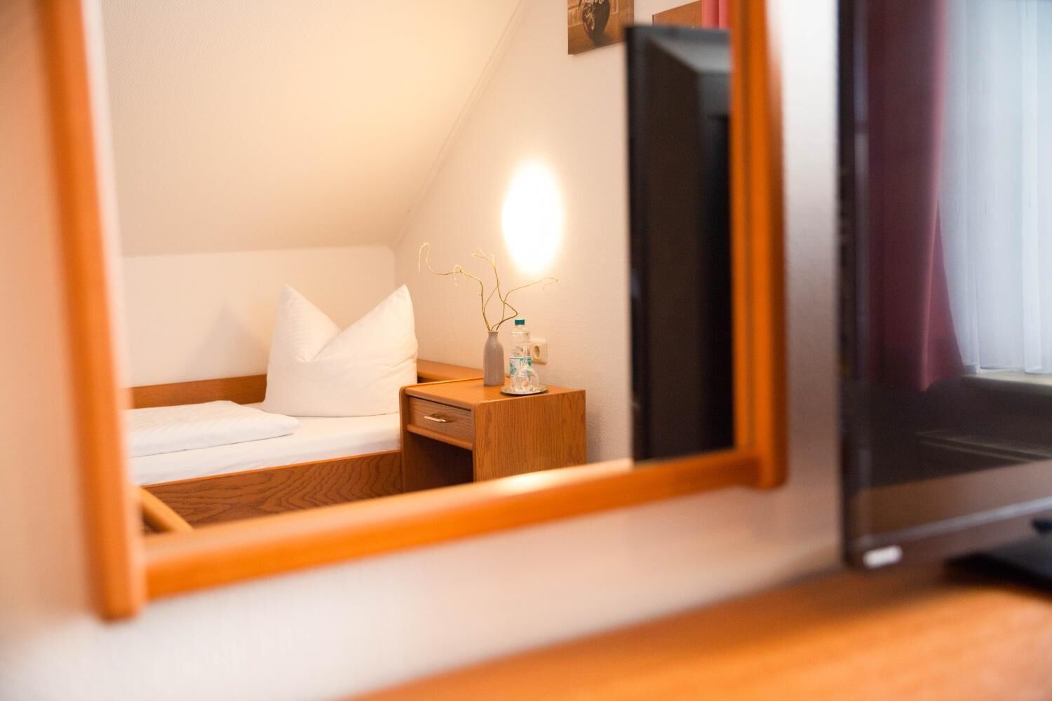 A hotel room with a bed, bedside table, and a mirror reflecting the room.