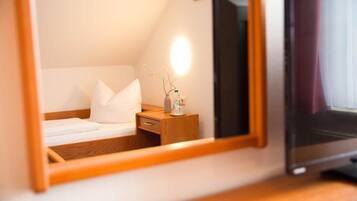 A hotel room with a bed, bedside table, and a mirror reflecting the room.