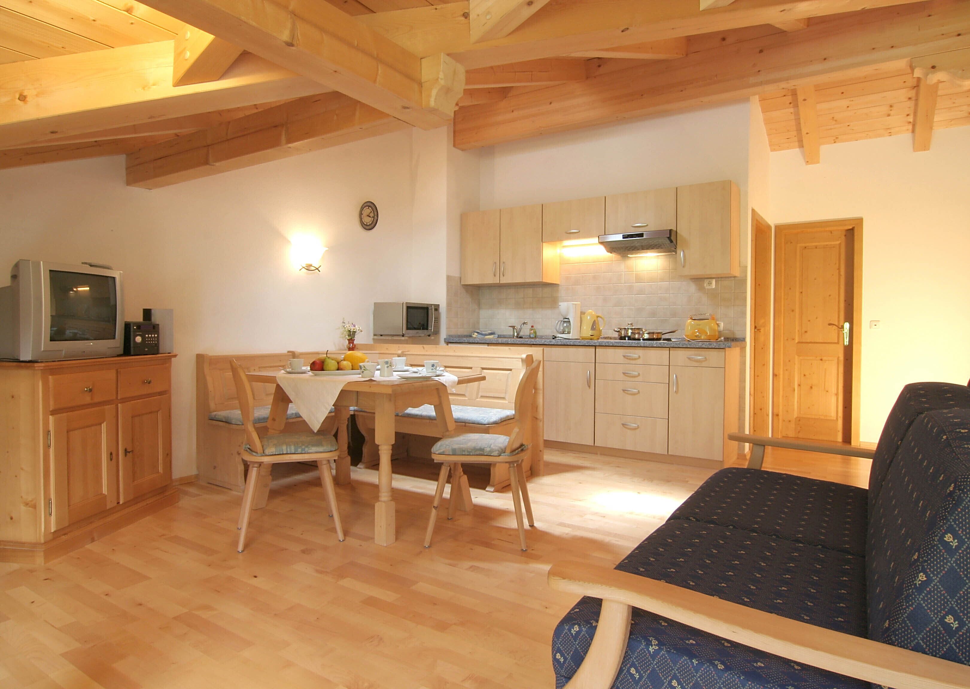 Una sala de estar acogedora con techo de madera, un comedor con mesa y sillas, y una cocina con armarios y electrodomésticos de madera.