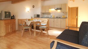 Una cocina acogedora con armarios de madera, una mesa de comedor con sillas, un televisor y un reloj en la pared.