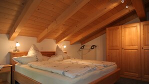 Un dormitorio con techo de madera, una cama con ropa de cama floral, lámparas de noche y un radiador.