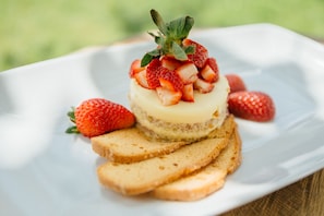 A dessert with a layered cake, strawberries, and biscuit pieces on a white plate.