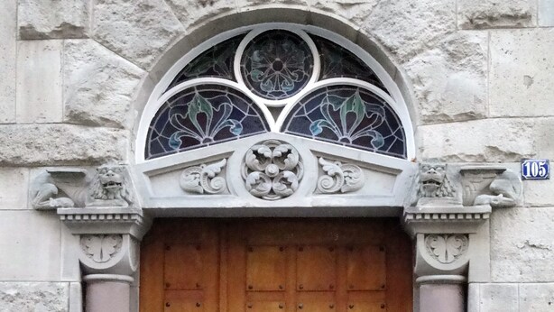 A stone building with a large wooden door, ornate window, and lion statues.